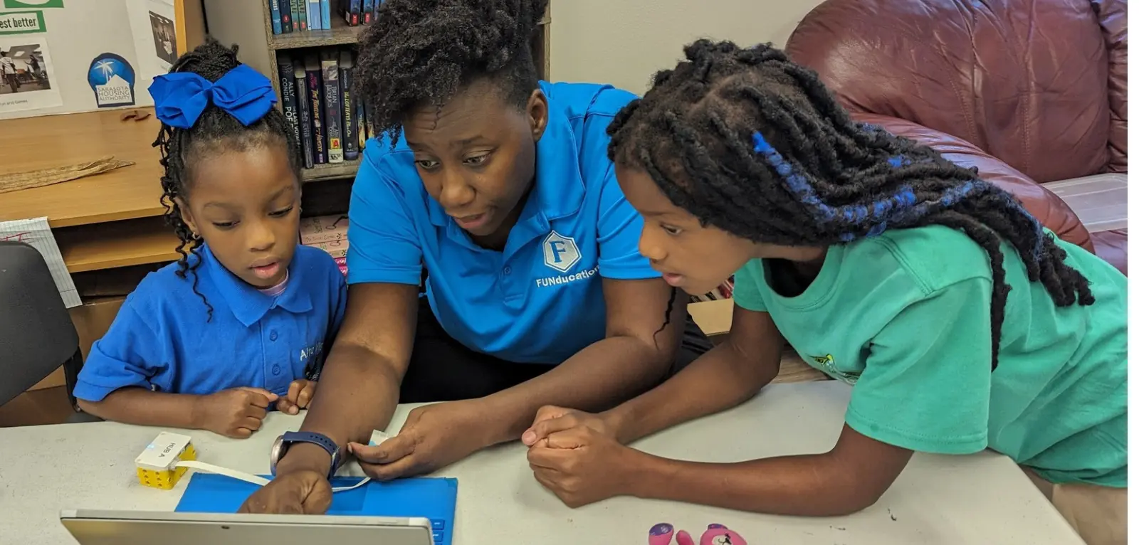 A woman helps two girls on a laptop