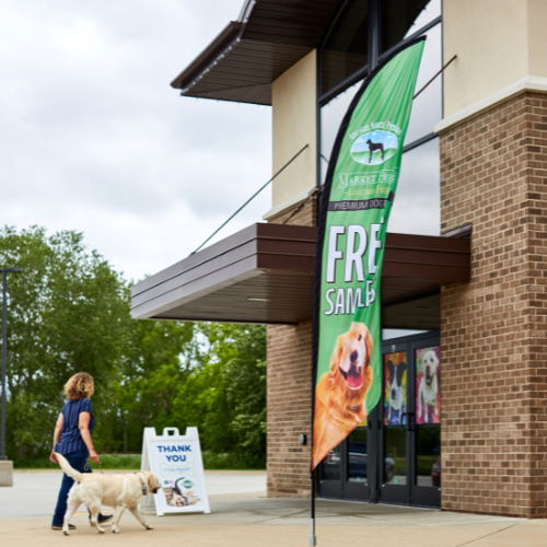 A feather flag and A-frame sign outside of a store advertise pet food