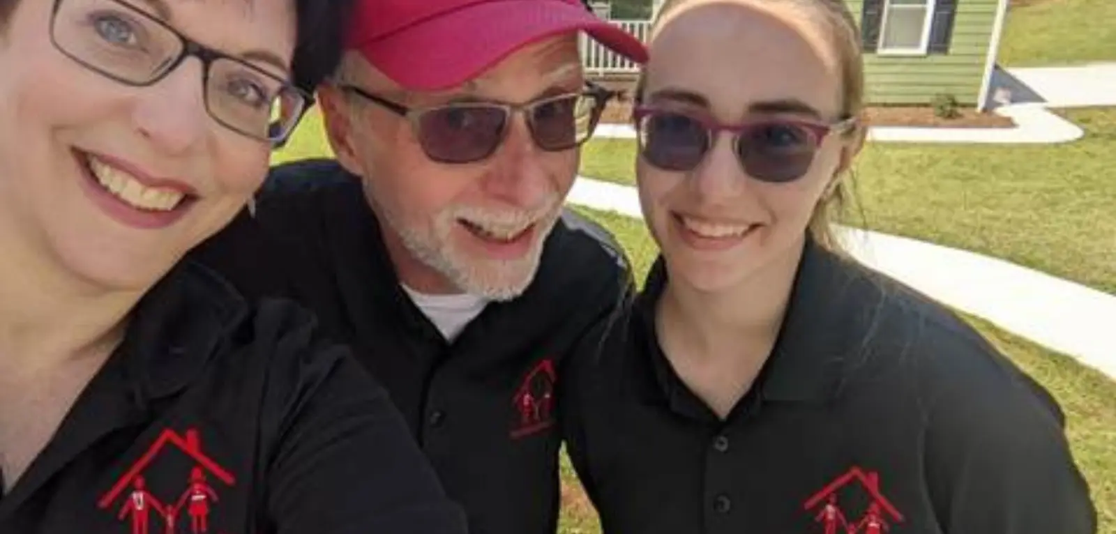 Two women and a man wear FamilyHomesGA polos and hats and smile for a selfie.