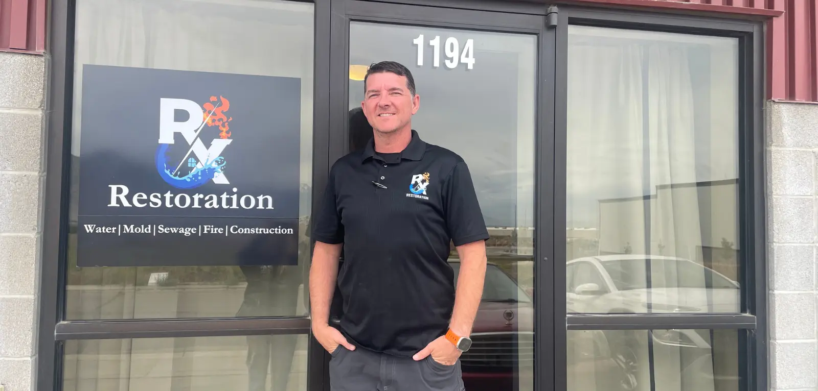 Man in black RX Restoration polo shirt stands in front of RX Restoration sign on a storefront